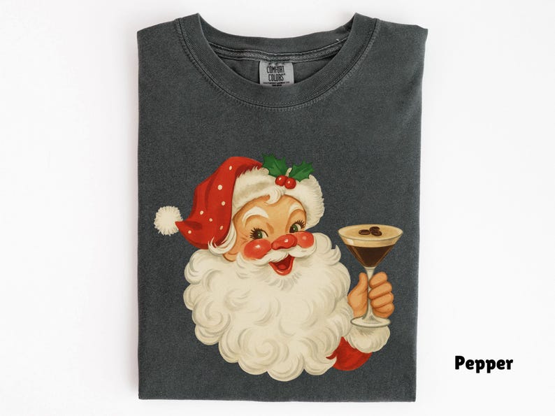 May include: Dark gray t-shirt featuring a vintage illustration of Santa Claus holding a martini. Santa is wearing a red hat with white polka dots and a white beard. The martini has coffee beans. The shirt is a Comfort Colors brand.