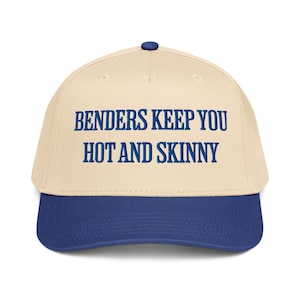 May include: A baseball cap with a cream-colored crown and a blue brim. The cap features the text "Benders Keep You Hot and Skinny" in blue block letters across the front. The cap has a blue button on top.