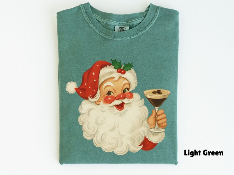 May include: Light green t-shirt featuring a vintage illustration of Santa Claus holding a cocktail. Santa is wearing a red hat with white trim and a white beard. The cocktail has coffee beans on top. The text "Light Green" is at the bottom right.