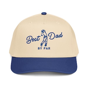 May include: A beige and navy blue baseball cap with the text "Best Dad BY PAR" in blue script. The cap features a golf-themed graphic of a golfer in mid-swing. The cap has a curved brim and a button on top.