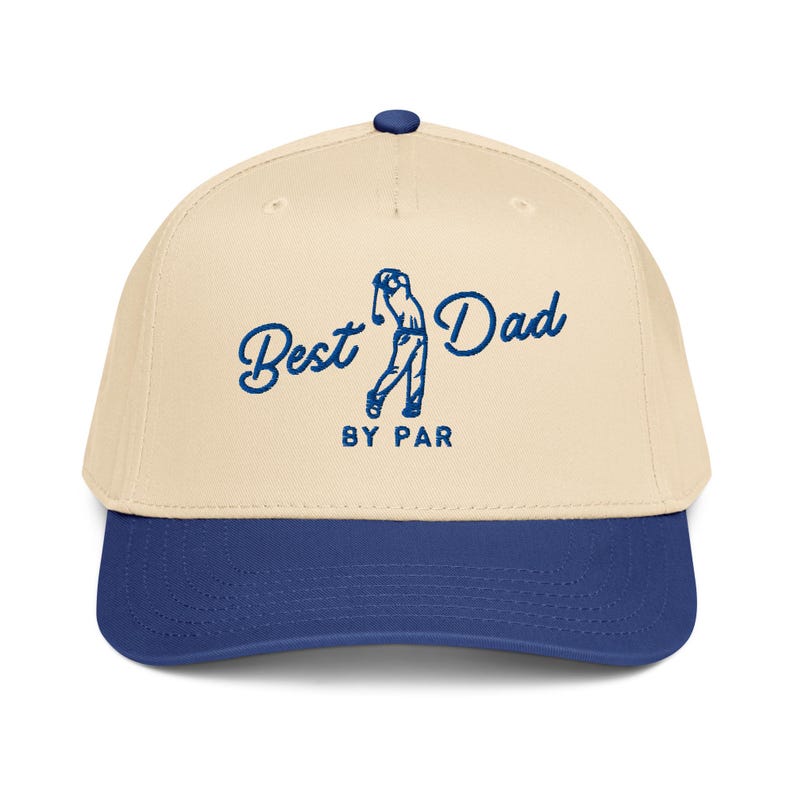 May include: A beige and navy blue baseball cap with the text "Best Dad BY PAR" in blue script. The cap features a golf-themed graphic of a golfer in mid-swing. The cap has a curved brim and a button on top.