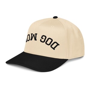May include: A baseball cap with a cream-colored crown and a black brim. The text "DOG MOM" is embroidered in black on the front of the cap. The cap has a curved brim and a small black button on top.