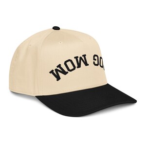 May include: A beige baseball cap with a black brim. The text "DOG MOM" is embroidered in black on the front of the cap. The cap has a curved brim and a button on top.