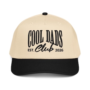 May include: A beige baseball cap with a black brim and a black button on top. The cap features the text "COOL DADS Club EST. 2026" in a bold, black font, making it a stylish accessory.