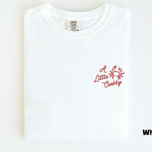 May include: White t-shirt with a red crab graphic and the text "A Little Crabby". The shirt is folded and has a crew neck. The shirt is made of a soft, comfortable material.