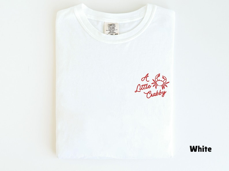 May include: White t-shirt with a red crab graphic and the text "A Little Crabby". The shirt is folded and has a crew neck. The shirt is made of a soft, comfortable material.