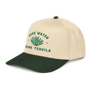 May include: A baseball cap with a cream-colored crown and a dark green brim. The cap features the text "SAVE WATER DRINK TEQUILA" in green, along with a green agave plant graphic. The cap has a dark green button on top.