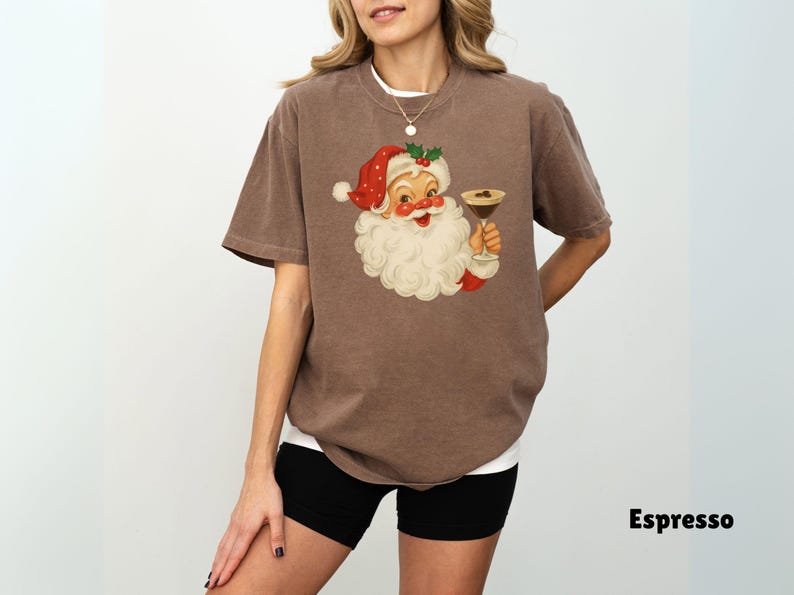 May include: Espresso-colored t-shirt featuring a vintage Santa Claus illustration holding a cocktail. Santa is wearing a red hat and suit with a white beard. The shirt is a casual style, perfect for the holiday season.