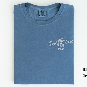 Pu&ograve; includere: Una maglietta blu jeans con le parole "Reel Cool Dad" ricamate in bianco. La maglietta &egrave; piegata ordinatamente e ha uno scollo tondo. La maglietta &egrave; una taglia XL.