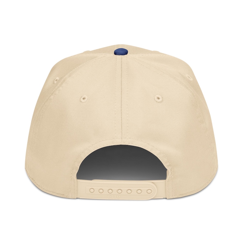 May include: A beige baseball cap with a navy blue button on top. The cap has a curved brim and an adjustable snapback closure. The hat is made of a durable fabric and features six ventilation eyelets.