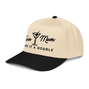 May include: A beige and black baseball cap with the text "Twin Mom, Make it a Double" in black script. The cap features a martini glass graphic and a curved brim.