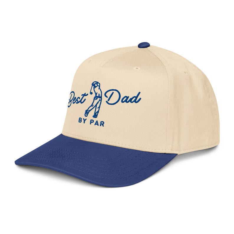 May include: A beige and blue baseball cap with the text "Best Dad BY PAR" in blue script. The cap features a golf-themed graphic and a curved brim.