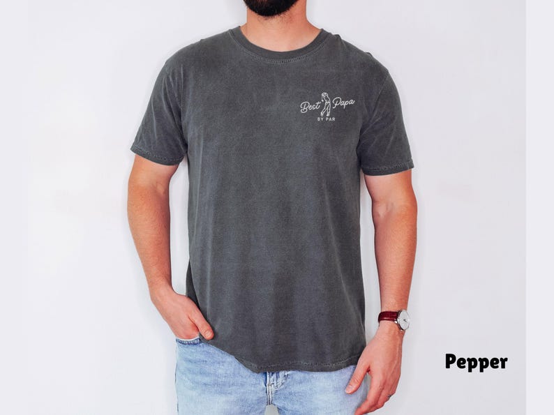 Op de afbeelding: Donkergrijs T-shirt met de tekst "Best Papa" en een golfclubafbeelding. Het shirt heeft een ronde hals en korte mouwen. De tekst "BY PAR" staat onder de afbeelding. Het shirt is gemaakt van zacht materiaal.
