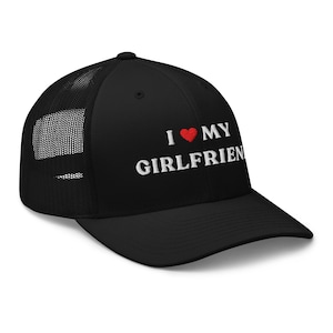 May include: Black trucker hat with a mesh back and a curved brim. The front of the hat features the embroidered text "I ❤️ MY GIRLFRIEN" in white, with a red heart symbol replacing the word "love".