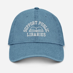 May include: Light blue denim baseball cap with the text "SUPPORT PUBLIC LIBARIES" embroidered in white above an open book graphic. The cap has a curved brim and an adjustable strap.