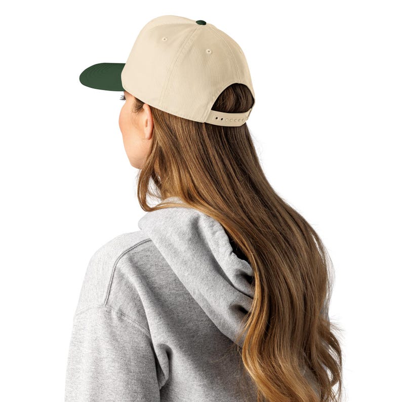 Puede incluir: Gorra de b&eacute;isbol beige con visera verde oscuro y bot&oacute;n negro en la parte superior. La gorra tiene una correa ajustable en la parte posterior. La gorra la lleva una persona con pelo largo casta&ntilde;o.