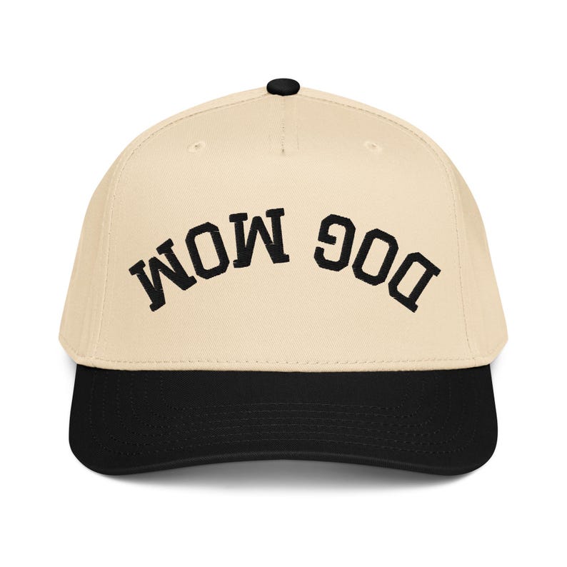 May include: A beige baseball cap with a black brim and a black button on top. The cap features the embroidered text "DOG MOM" in black, arched across the front. This hat is a stylish accessory for dog lovers.