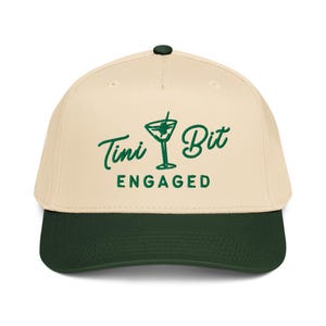 Puede incluir: Gorra de b&eacute;isbol con corona color crema y visera verde oscuro. La gorra presenta las palabras "Tini Bit Engaged" en verde, junto con una ilustraci&oacute;n de una copa de martini. Bot&oacute;n verde oscuro en la parte superior.