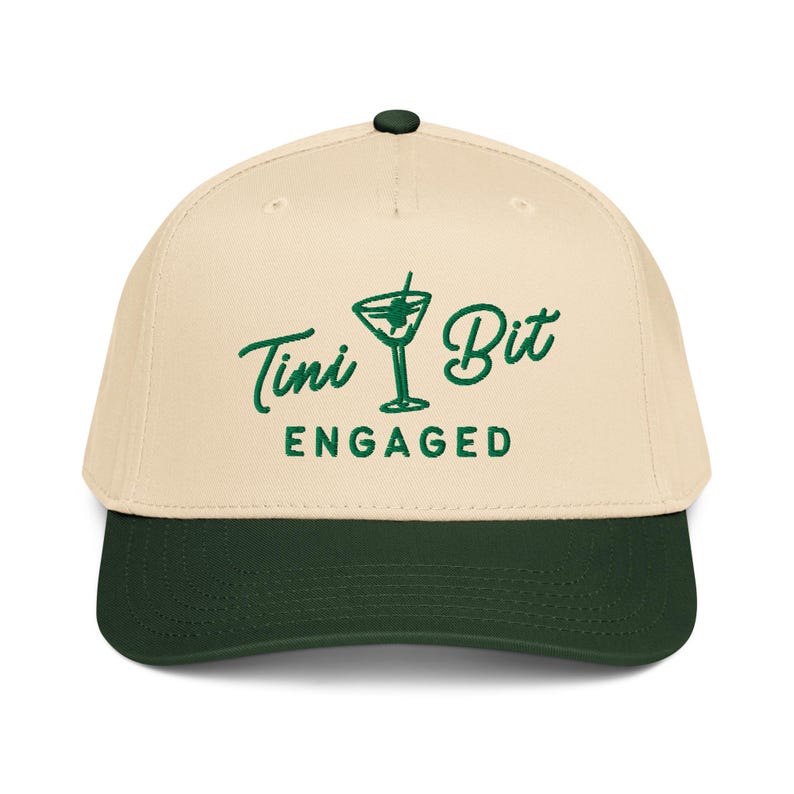 Puede incluir: Gorra de b&eacute;isbol con corona color crema y visera verde oscuro. La gorra presenta las palabras "Tini Bit Engaged" en verde, junto con una ilustraci&oacute;n de una copa de martini. Bot&oacute;n verde oscuro en la parte superior.