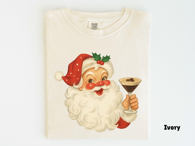 May include: Ivory-colored t-shirt featuring a vintage illustration of Santa Claus holding a cocktail. Santa is depicted with a red hat with white polka dots, a white beard, and rosy cheeks. The cocktail has coffee beans.