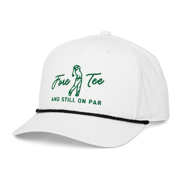 May include: White baseball cap with a black rope detail and a curved brim. The cap features the text "Fore Tee" in green script with a golf player graphic, and the phrase "AND STILL ON PAR" below.