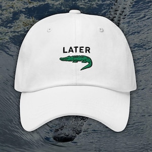 Puede incluir: Gorra de b&eacute;isbol blanca con la palabra "LATER" en letras negras y un gr&aacute;fico de un cocodrilo verde. La gorra tiene una visera curva y una correa ajustable, un dise&ntilde;o cl&aacute;sico de seis paneles.