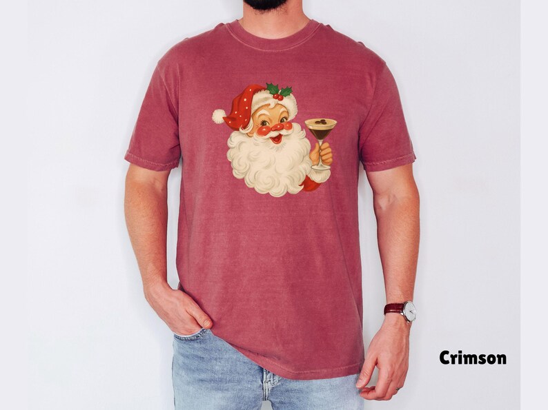 May include: Crimson-colored t-shirt featuring a vintage illustration of Santa Claus holding a cocktail. Santa is depicted with a white beard, red hat, and a jolly expression. The shirt is a solid color with the word "Crimson" printed in black.
