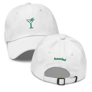 May include: White baseball cap with a green embroidered martini glass on the front. The back of the cap features the word "Auntini" in green. The cap has a curved brim and an adjustable strap.