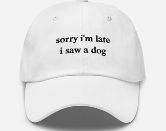May include: White baseball cap with a curved brim. The cap features the text "sorry I'm late i saw a dog" in black, centered on the front. The cap has a classic six-panel design with a button on top.