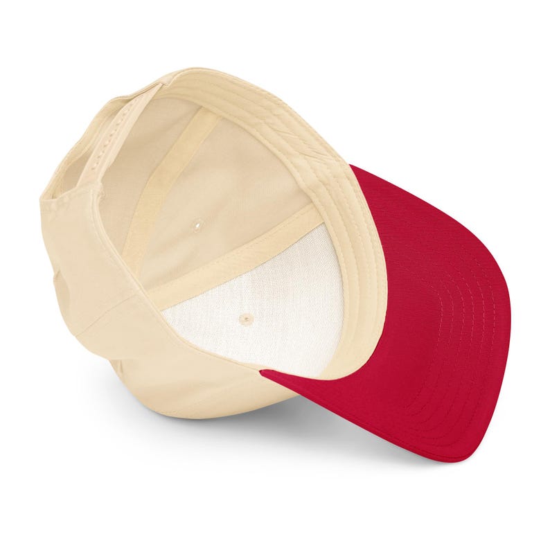 May include: A cream-colored baseball cap with a red brim. The interior of the cap is cream-colored with a white lining. The cap has an adjustable strap at the back.