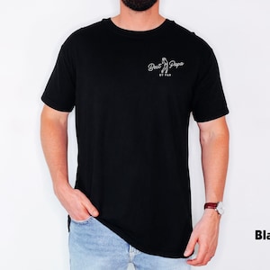 Op de afbeelding: Zwart T-shirt met de tekst "Best Papa" en een witte golfclubafbeelding. Het shirt is gemaakt van een zacht materiaal en is geschikt voor vrijetijdskleding. De tekst is wit en het shirt wordt door een persoon gedragen.