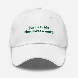 May include: White baseball cap with the text "just a bride that loves a marg" in green lettering. The cap has a curved brim and a six-panel design, suitable for casual wear.