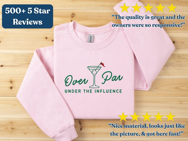 May include: Light pink sweatshirt with the text "Over Par UNDER THE INFLUENCE" in green, featuring a martini glass with a golf flag. The sweatshirt has long sleeves and includes customer reviews.