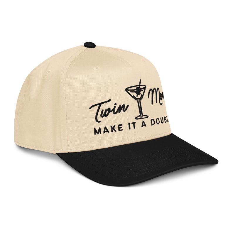 May include: A beige baseball cap with a black brim. The cap features the text "Twin Mom" and "Make it a Double" in black script, along with a martini glass graphic. The cap has a curved bill and a button on top.