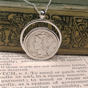 May include: A silver necklace with a round pendant featuring a 1938 Walking Liberty half dollar coin. The coin is suspended within a silver circle, allowing it to rotate freely.