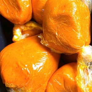 May include: Several orange-colored food items are wrapped in clear plastic wrap. The food items are in a black container.