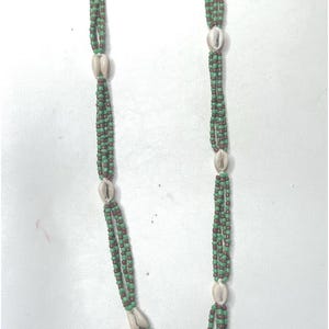 Puede incluir: Un collar de múltiples hilos hecho de cuentas verdes y marrones con detalles de conchas blancas. El collar tiene un borla en la parte inferior.