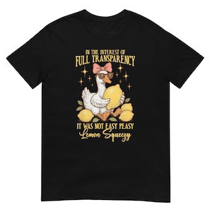May include: Black t-shirt with a cartoon goose wearing sunglasses and a pink bow, holding a lemon. Text reads "IN THE INTEREST OF FULL TRANSPARENCY" and "IT WAS NOT EASY PEASY Lemon Squeezy". The design includes lemons and stars.