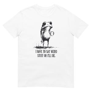 May include: White t-shirt featuring a black and white illustration of a frog holding a mug. The frog has a quirky expression. Below the frog is the text: "I HAVE TO SAY WEIRD STUFF OR I'LL DIE."
