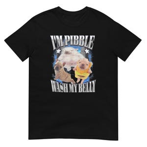 May include: Black t-shirt with a graphic design. The design features the text "I'M PIBBLE WASH MY BELLY" and three cartoon dogs. One dog is wearing a yellow outfit. The design has a distressed, vintage appearance.