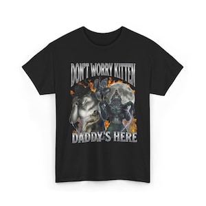 May include: Black t-shirt with the text "DON'T WORRY KITTEN DADDY'S HERE" in a silver, metallic style. The graphic includes illustrations of werewolves, a full moon, and flames.