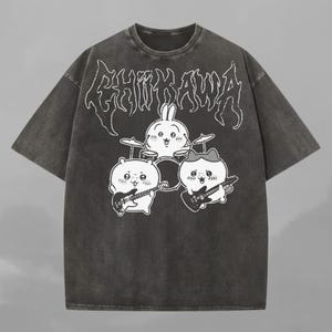 Peut inclure: T-shirt gris foncé avec une illustration d'un groupe de dessins animés. Le groupe comprend un lapin à la batterie et deux autres personnages jouant de la guitare. Le texte "CHIIKAWA" est imprimé au-dessus du groupe dans une police stylisée.