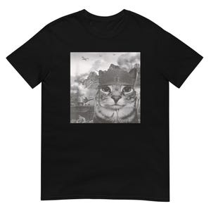 Może przedstawiać: Czarny t-shirt z szarą grafiką kota w wojskowym hełmie, na tle sceny wojennej z górami i samolotami. Twarz kota jest centralnym punktem.