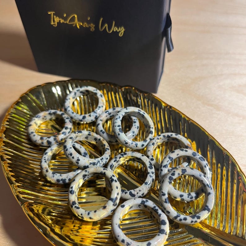 May include: A collection of dalmatian jasper rings in a gold leaf dish. The rings are all different sizes and have a speckled pattern of black and white.