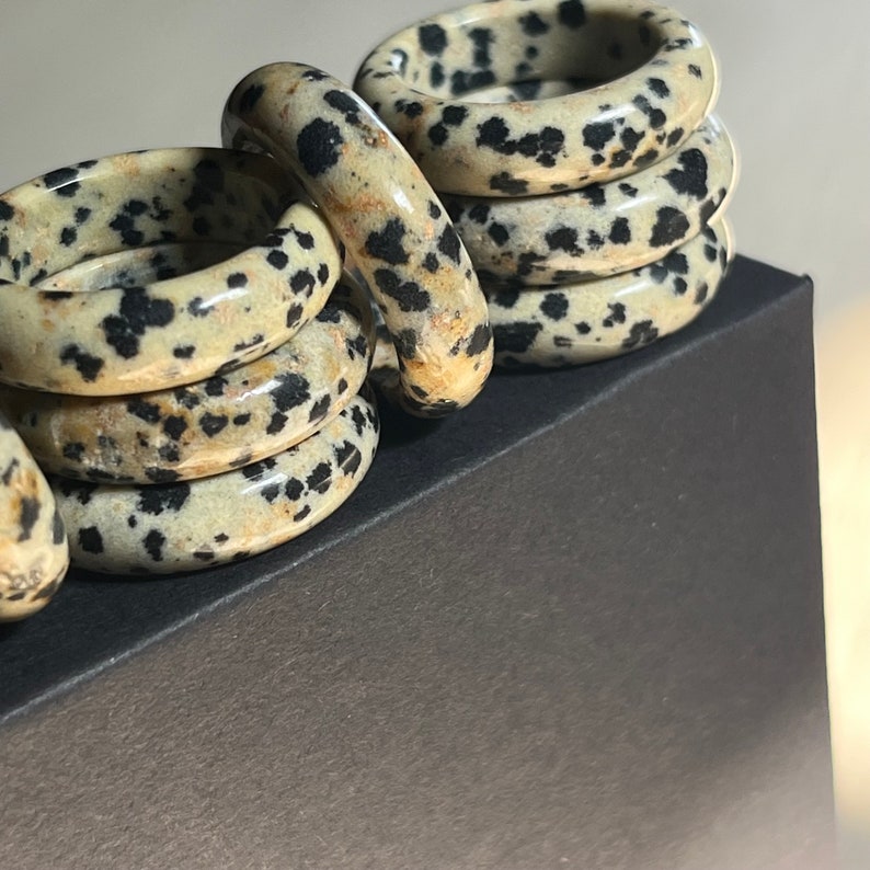 May include: A stack of six rings made of dalmatian jasper, a stone with a white and black speckled pattern. The rings are stacked on a black surface.