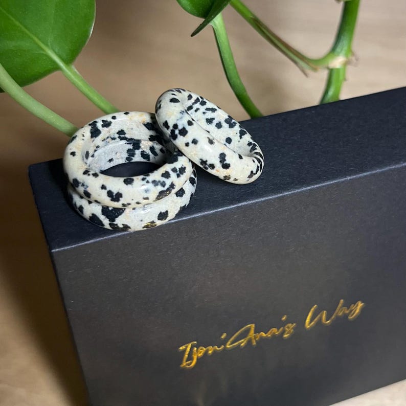 May include: Three black and white speckled rings stacked on top of each other on a black box with the text "Tyoni Anais Way" in gold lettering.