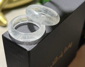 May include: Two clear white crystal rings with a cloudy, textured appearance. The rings are stacked on top of each other and are sitting on a black box.