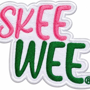 May include: A white embroidered patch with a scalloped edge featuring the text SKEE in pink and WEE in green. The letters are stitched in a bold, rounded font against a white fabric background, with a small registered trademark symbol.