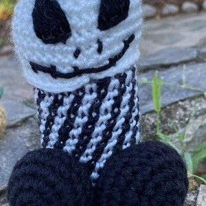 May include: A handmade crochet figure resembling Jack Skellington from The Nightmare Before Christmas. The figure features a white head with black eyes and a stitched smile, a black and white striped body, and two black spheres at the base.