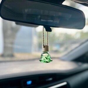 Pode incluir: Um aromatizador de carro de vidro verde em forma de rosa pendurado no espelho retrovisor de um carro.
